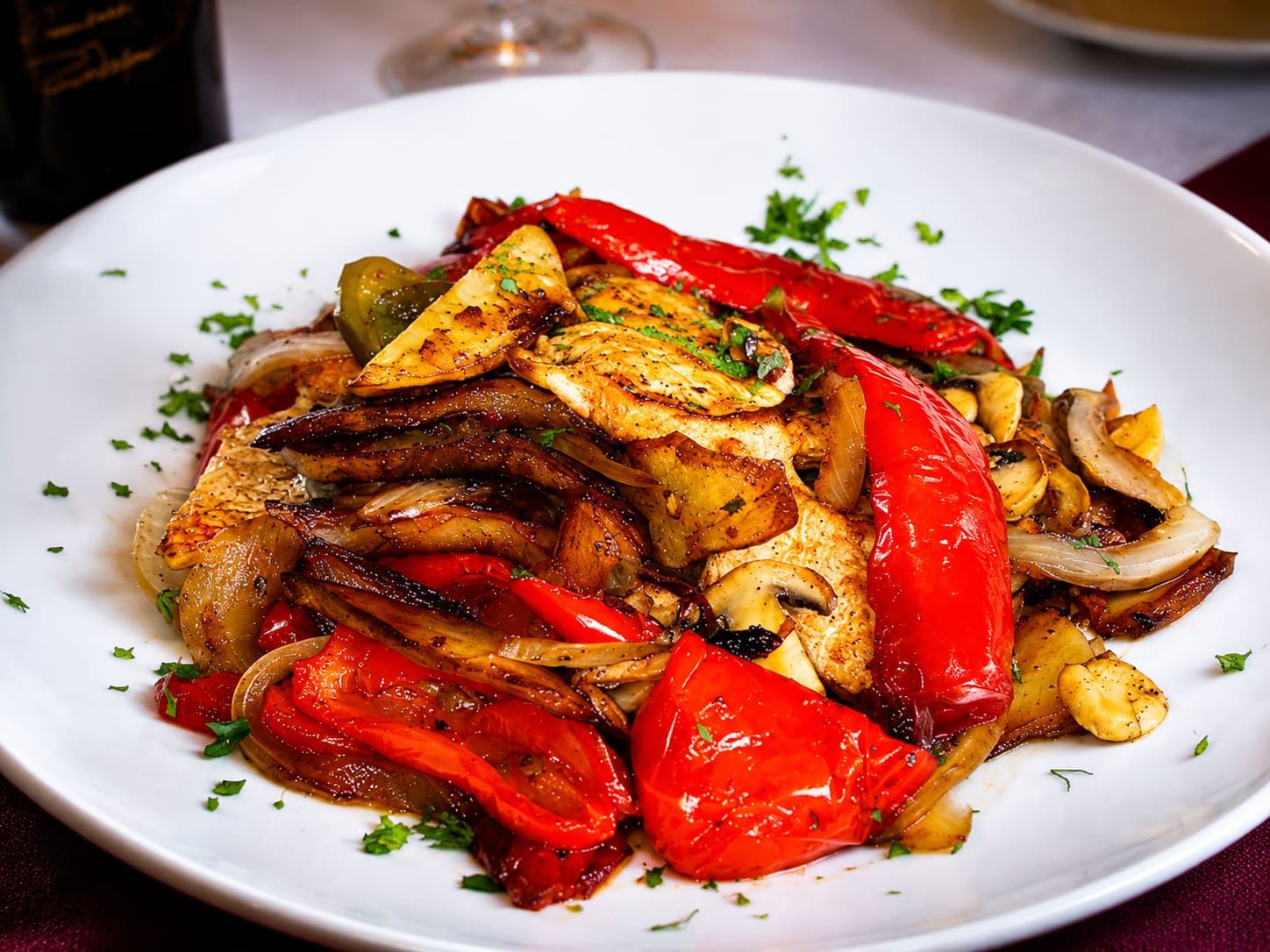 Chicken Campagna — sliced chicken breast tossed with roasted red peppers, sliced onions, mushrooms and browned potato wedges on a white plate, scattered with parsley.
