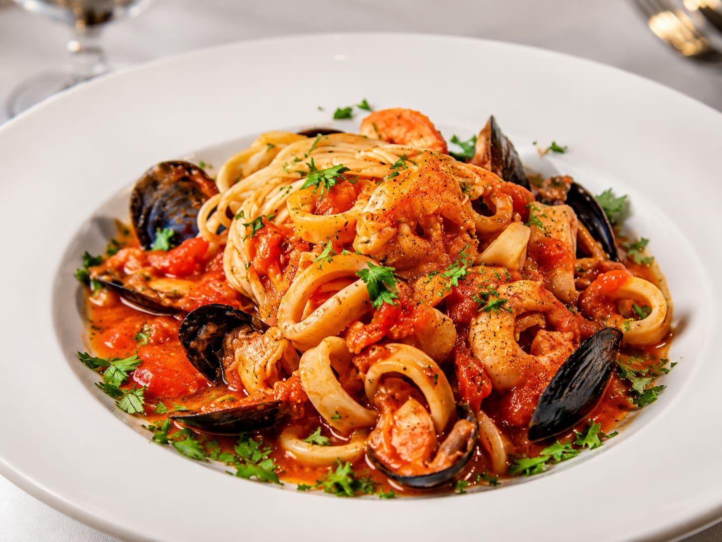 Frutti di mare — long flat pasta tangled with calamari rings, black-shelled mussels and shrimp in a chunky red tomato sauce, under black pepper and chopped parsley.