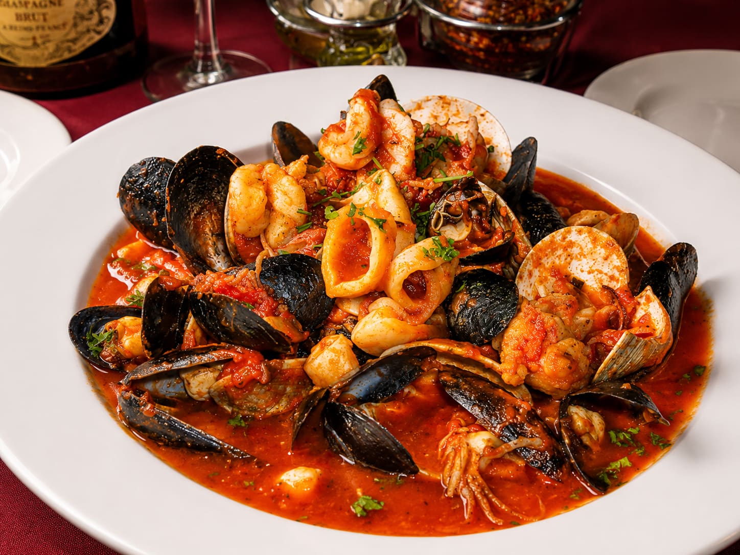 A wide bowl of mussels, opened clams, calamari rings and shrimp in a brothy red tomato sauce, scattered with parsley.